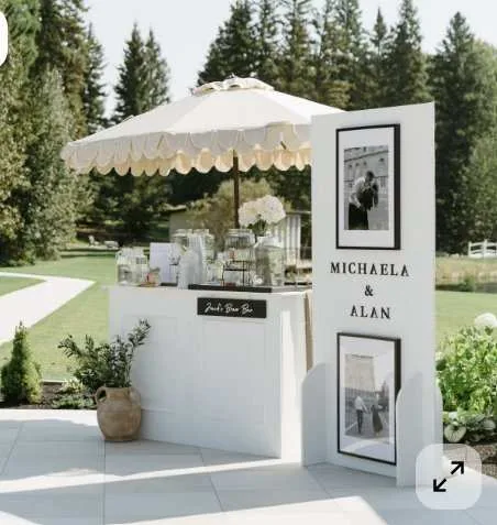 Bar d'accueil blanc avec parasol festonné et panneau photo