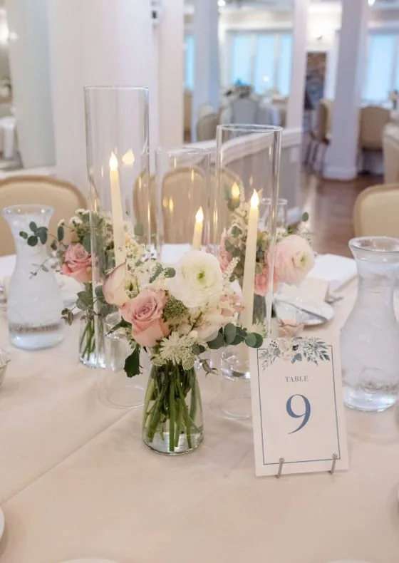 Centre de table : roses poudrées et renoncules en fioles, hauts vases et bougies